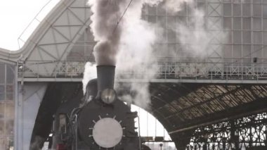 Retro buhar treni tren istasyonundan ayrılıyor. Mavi arabalı eski siyah buhar treni