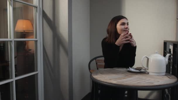 Ung vacker kvinna sitter hemma i stol vid fönster med kopp varmt kaffe — Stockvideo