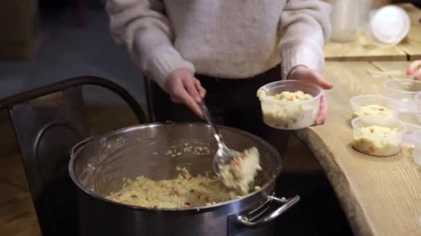Primo piano di una mano di donne che raccoglie il porridge di riso da grande vaso in ciotole di plastica — Video Stock