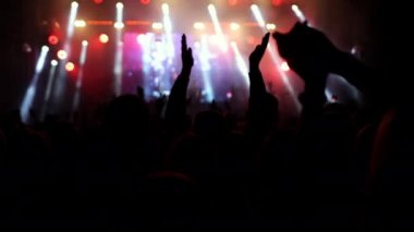 Parlak sahne ışıkları önünde konser kalabalığı siluetleri. İnsanların silueti