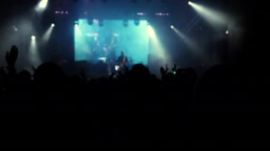 Parlak sahne ışıkları önünde konser kalabalığı siluetleri. İnsanların silueti