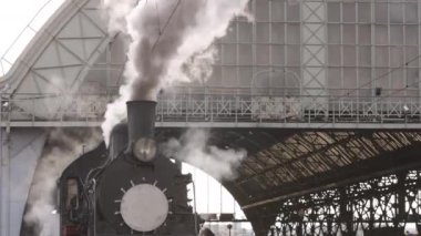 Retro buhar treni tren istasyonundan ayrılıyor. Mavi arabalı eski siyah buhar treni