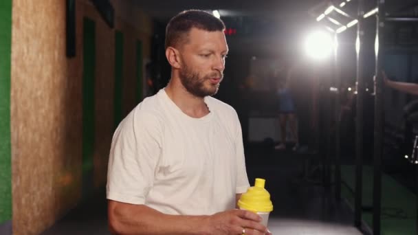 Lifestyle-Porträt eines muskulösen Mannes, der Wasser in der Turnhalle trinkt. Hübscher Nachwuchs löscht Durst — Stockvideo