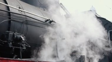 Treni kaplayan duman. Retro buharlı lokomotif tren istasyonundan ayrılıyor. Eski siyah buhar treni