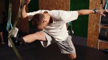 Fit bir genç adam uçuş yogası yapıyor spor yaparken trx fitness kayışlarıyla esneme egzersizleri yapıyor.