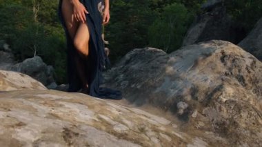 Ayağını kayaya koy. Yakın plan. Kadın, rüzgarda uçuşan bir elbiseyle kayaların arkasına doğru uçarken görülüyor. Romantizm, seyahat ve turizm kavramı.