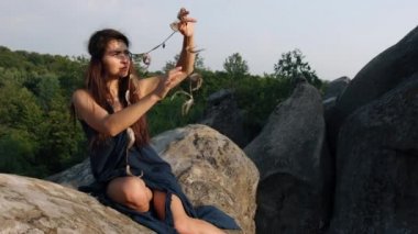 Yaşlı kadın uçurumun kenarında oturuyor, saçın içine örülmüş tüylere bakıyor. Kayanın kenarındaki güzel elbiseli genç bayan. Düşünme zamanı ve kendi kendine özümseyen fikir