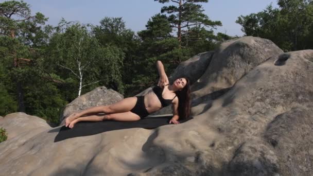 漂亮的女人在垫子上伸展着她的身体 抬起她的胳膊和腰部 美丽的女士早上在岩石上做运动 — 图库视频影像