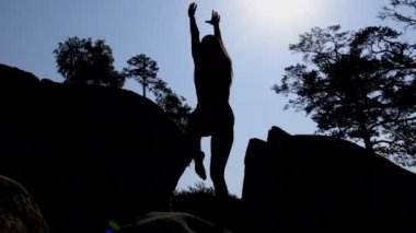 Güzel bir kadın silueti bir bacağının üzerinde dengede duruyor ve bir uçuruma tırmanıyor. Şafak vakti kayalık arazide genç ve güzel bir bayan antrenman yapıyor. Spor giyim bölümündeki güzel formalı kız dışarıda Rocky 'de egzersiz yaparken..