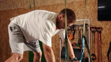 Süspansiyon askısı takan bir adam. Trx 'i tutarken havada şınav çeken genç bir adam. Güzel erkek, uçuş yogası yapıyor. Egzersiz yapıyor. Antrenmanlarda spor kayışlarıyla esnetiyor.