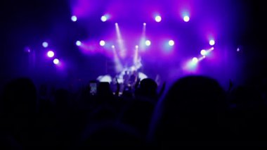 Parlak ışıkların önünde rock resitalinde tezahürat yapan kalabalık. Parlak sahne ışıkları önünde konser kalabalığı siluetleri. Rock konseri, tezahürat yapan kalabalık, çok renkli sahne