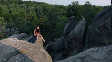 Mavi elbiseli vahşi ortaçağ kadını Camus Rock 'ın kenarına oturmuş ve kendini okşuyor. Güneşe bakmak yalnızlık konseptidir. Ormanın arkasında.