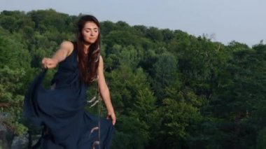 Vahşi kadın elbise giyer, güneşe bakar. Kadın, rüzgarda dalgalanan bir elbiseyle kayaların arkasında görülmüş. Romantizm, seyahat ve turizm kavramı.