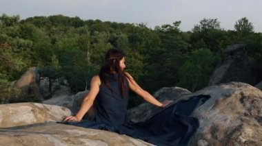 Arkadan kadın, rüzgarda dalgalanan bir elbiseyle kayaların arkasında görülüyor. Romantizm, seyahat ve turizm kavramı.