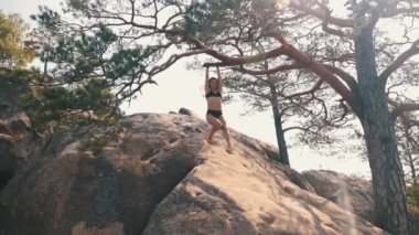 Kadın sallanıyor, elleri ile ağaç dalına tutunuyor kayalık arazide güneşin doğuşunu seyrediyor. Genç bayan kayaların üzerinde dinleniyor. Özgürlük, rahatlama, tatil, seyahat kavramı.