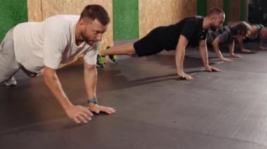 Tam uzunluktaki şut grupları atletleri şınav çekerken başka yöne bakıyorlar. Eğitim, aktif yaşam tarzı, takım konsepti. Yatay çekim. Spor salonunda şınav çeken zinde gençler odaklanmış görünüyorlar.