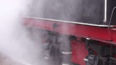 Treni kaplayan duman. Retro buharlı lokomotif tren istasyonundan ayrılıyor. Eski siyah buhar treni çok duman çıkarıyor. Tarihi turu olan klasik bir lokomotif. Yakın plan.
