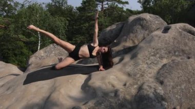 Güzel bir kadın vücudunu paspasa dayar ve bacağını ve belini kaldırır. Güzel bir bayan sabah kayanın üstünde egzersiz yapıyor..