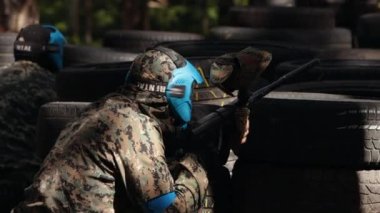 Savaş alanında paintball oynayan neşeli yetişkin insanların portresi. Savaş oynamak için özel koruyucu maske. Paintball oyuncusu nişan alıyor. İnsan lastiklerin arkasında düşmandan saklanır.