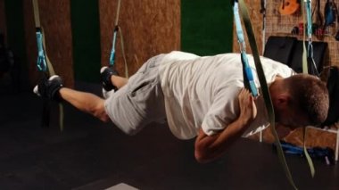 Süspansiyon askısı takan bir adam. Trx 'i tutarken havada şınav çeken genç bir adam. Eğitimdeki spor kayışlarıyla sinek yogası esneme egzersizleri yapan yakışıklı bir erkek. Atlet durdu.