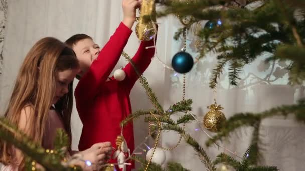 クリスマスツリー ハンギングオーナメント 女の子と男の子を飾るユリテのシンボルにおもちゃを身に着けています 弟と妹はクリスマスツリーの装飾にしがみつく — ストック動画