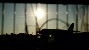 Gün batımında bir uçağın karanlık silueti havaalanına yaklaşıyor güzel bir gökyüzü, uçaklar. Önplanda bariyer ızgarası