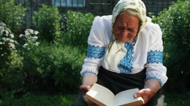 Yaşlı bir büyükanne sokakta oturuyor ve bir kitap okuyor. Vyshyvanka Ulusal Ukrayna giysileri giyiyor.