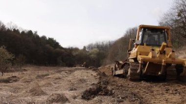 İnşaat alanındaki buldozer bir yığın toprağa toprak topluyor. Güçlü sarı toprak taşıyıcı ereksiyon alanında kumu parçalar. Yolu döşemek için buldozer, ticari araç..