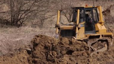 İnşaat alanındaki buldozer bir yığın toprağa toprak topluyor. Güçlü sarı toprak taşıyıcı ereksiyon alanında kumu parçalar. Yolu döşemek için buldozer, ticari araç..