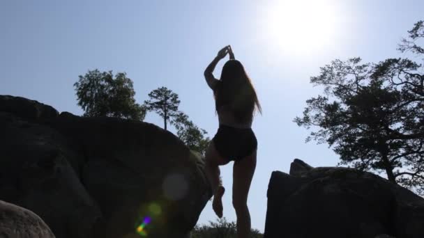 漂亮女人的轮廓在一条腿上保持平衡能爬上悬崖 年轻美丽的女运动员黎明时分在岩石地形上训练 在外面岩石上锻炼时穿着运动服的漂亮姑娘 — 图库视频影像