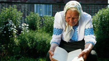 Yaşlı bir büyükanne sokakta oturuyor ve bir kitap okuyor. Vyshyvanka Ulusal Ukrayna giysileri giyiyor.