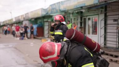 Group of firefighters preparing for a drill, firefighter in protective gear with a helmet on his head checking his equipment, a fire truck in the background is also visible