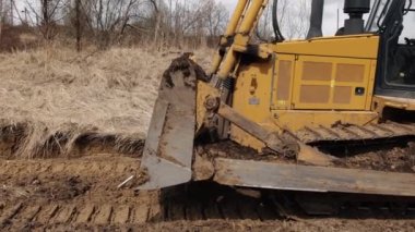 İnşaat alanındaki buldozer bir yığın toprağa toprak topluyor. Güçlü sarı toprak taşıyıcı ereksiyon alanında kumu parçalar. Yolu döşemek için buldozer, ticari araç. Kapat.