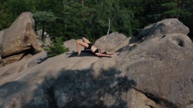 Güzel bir kadın mindere uzanır, leğen kemiğini, vücudunu, ellerini kaldırır. Güzel bir bayan sabah kayanın üstünde egzersiz yapıyor..
