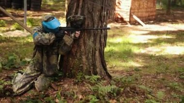 Man wears camouflage and protective mask while participating in a paintball battle game with friends, takes part in leisure activities.