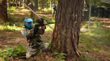 Young man playing the game of paintball with his friends. Wearing camouflage and protective mask, engaged in leisure activity. Raised his hands in the air and give up
