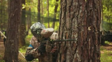 Playing paintball battles with his friends while wearing camouflage and protecting mask, an enjoyable leisure activity.