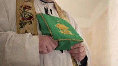 Catholic priest in cassock holds bag with image of symbols of faith fish and wine. A Christian ritual. Close-up