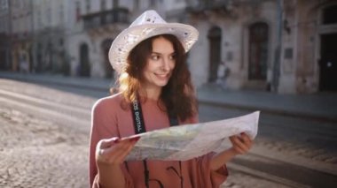Young woman exploring beautiful sights in Europe, slow motion, hipster girl holding tourist map, enjoying holiday, lady walking down street, using paper map in old town to find her way. Go Everywhere