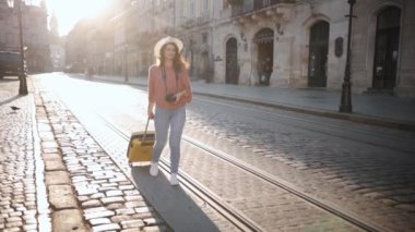 Female tourist walking with suitcase on wheels around city a old buildings, female student walking the street, suitcases with luggage, enjoy travel, vacation destination, Caucasian lady. Go Everywhere