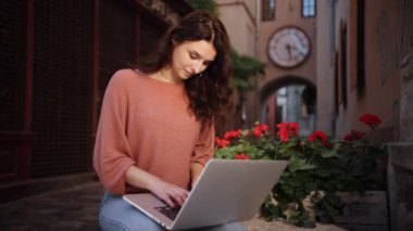 Woman typing on a laptop keyboard while sitting on decorative stones of city streets, A pretty young female using a laptop, girl student preparing for classes in nature, adult woman studying outdoors
