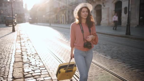 魅力的な若い観光客は 車輪の上のスーツケース 通りを歩いている女性学生 荷物付きのスーツケース 休暇先をお楽しみください どこへでも — ストック動画