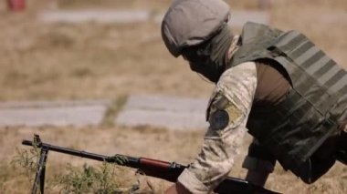 An army man in a green uniform vest is unloading a machine gun, lying on ground with a weapon, ready to attack, machine gun crew of corps is firing, and army gunner is firing at enemy.