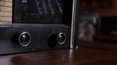 Radyo alıcısı ahşap masa üzerinde takriben 1950 model ön plan, müzik konsepti, eski tarz, fm kanalı müzik çalıyor, retro radyo çalgıcısı duruyor, el kapatması radyoyu açıyor