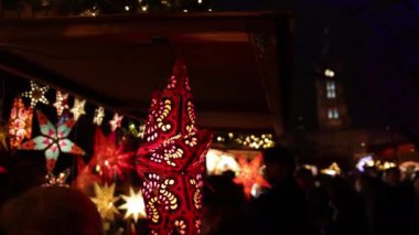 Noel yıldızı ön planda asılı duruyor. Açık hava ampul dekoru, açık hava aydınlatması, Noel pazarında hediyeler ve mallar satılıyor.
