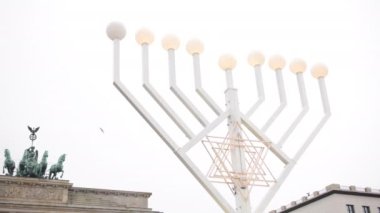 Yahudiler Hanukkah 'ı, Almanya' da Berlin 'de geleneksel şamdanlar ve mumlarla dışarıda parıldayan sokak lambalarıyla yakarak kutluyorlar. Brandenburg kapısı arka planda.