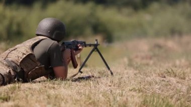 Military man in green uniform vest unloading gun with machine gun in hand, soldier lying on ground with gun, officer firing machine gun, Army gunner attacking, Army war concept.