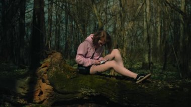 Yaz ormanındaki ağaçta yalnız bir kız deftere yazı yazar ve sevinir.