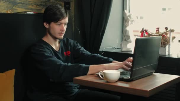 Hombre de diseñador independiente adulto joven trabaja en una computadora portátil en un café de la mañana — Vídeos de Stock