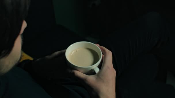 Νεαρός καυκάσιος πίνει καφέ από ένα άσπρο φλιτζάνι σε ένα σκοτεινό καφέ. — Αρχείο Βίντεο